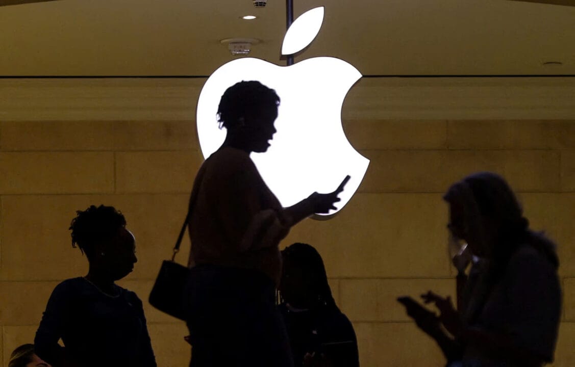 Người phụ nữ sử dụng thiết bị di động iPhone của mình khi cô ấy đi qua logo Apple phát sáng tại cửa hàng Apple ở New York